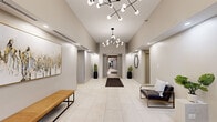 Located at 149 Forest Ave in Oak Park, Illinois, this single-floor lobby space presents a thoughtfully designed, contemporary environment that makes a strong first impression. The entryway opens into a spacious, light-filled corridor characterized by large-format white tile flooring that extends throughout, lending a clean and cohesive aesthetic to the entire space.

Soaring ceilings amplify the sense of openness, and are complemented by striking sputnik-style chandeliers featuring globe bulbs arranged on geometric frames—serving as standout design focal points. Recessed lighting throughout adds layered illumination, ensuring the space feels bright and welcoming.

The corridor leads seamlessly between distinct areas, including a seating alcove furnished with sleek leather and wood-frame chairs and a tan leather bench. Curated décor such as abstract framed artwork, a geometric hexagonal wall mirror, potted snake plants in matte black planters, and a textured area rug add warmth and personality to the otherwise neutral palette.

An elevator vestibule features a bold abstract wall mural in warm gold and grey tones, paired with a patterned runner rug and bench seating. The lobby connects to glass-paneled entry doors, allowing natural light to filter in and providing views to the exterior. The overall ambiance is polished, modern, and welcoming.