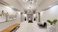 Located at 149 Forest Ave in Oak Park, Illinois, this single-floor lobby space presents a thoughtfully designed, contemporary environment that makes a strong first impression. The entryway opens into a spacious, light-filled corridor characterized by large-format white tile flooring that extends throughout, lending a clean and cohesive aesthetic to the entire space.

Soaring ceilings amplify the sense of openness, and are complemented by striking sputnik-style chandeliers featuring globe bulbs arranged on geometric frames—serving as standout design focal points. Recessed lighting throughout adds layered illumination, ensuring the space feels bright and welcoming.

The corridor leads seamlessly between distinct areas, including a seating alcove furnished with sleek leather and wood-frame chairs and a tan leather bench. Curated décor such as abstract framed artwork, a geometric hexagonal wall mirror, potted snake plants in matte black planters, and a textured area rug add warmth and personality to the otherwise neutral palette.

An elevator vestibule features a bold abstract wall mural in warm gold and grey tones, paired with a patterned runner rug and bench seating. The lobby connects to glass-paneled entry doors, allowing natural light to filter in and providing views to the exterior. The overall ambiance is polished, modern, and welcoming.