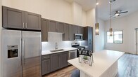 Located in Scottsdale, Arizona, this thoughtfully designed one-bedroom, one-bathroom residence offers a well-appointed layout with modern finishes throughout. The open-concept kitchen serves as a focal point, featuring floor-to-ceiling gray shaker cabinetry, a white quartz countertop island with pendant lighting, a decorative geometric tile backsplash, and a full suite of stainless steel appliances including a gas range, dishwasher, microwave, and refrigerator with ice maker. Soaring ceilings amplify the sense of openness in the main living area, which is complemented by warm wood-look flooring. The bedroom offers plush carpeting, a large window with views of the surrounding community, and a stylish barn-style sliding door leading to a closet. A second room with wood-look flooring and a large window provides additional versatile space. The bathroom is well-equipped with gray cabinetry, white quartz countertops, a glass-enclosed walk-in shower, and direct access to a walk-in closet. Clean white walls and consistent modern hardware tie the design together, creating a cohesive and contemporary living environment in one of Scottsdale's desirable communities.