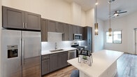 Located in Scottsdale, Arizona, this thoughtfully designed one-bedroom, one-bathroom residence offers a well-appointed layout with modern finishes throughout. The open-concept kitchen serves as a focal point, featuring floor-to-ceiling gray shaker cabinetry, a white quartz countertop island with pendant lighting, a decorative geometric tile backsplash, and a full suite of stainless steel appliances including a gas range, dishwasher, microwave, and refrigerator with ice maker. Soaring ceilings amplify the sense of openness in the main living area, which is complemented by warm wood-look flooring. The bedroom offers plush carpeting, a large window with views of the surrounding community, and a stylish barn-style sliding door leading to a closet. A second room with wood-look flooring and a large window provides additional versatile space. The bathroom is well-equipped with gray cabinetry, white quartz countertops, a glass-enclosed walk-in shower, and direct access to a walk-in closet. Clean white walls and consistent modern hardware tie the design together, creating a cohesive and contemporary living environment in one of Scottsdale's desirable communities.