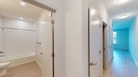 This single-floor unit offers a clean, contemporary design with a thoughtful layout that maximizes functionality. The open-concept kitchen and living area serves as the heart of the space, featuring light hardwood-style flooring, a large window that draws in natural light and provides views of the surrounding area, and a track lighting system overhead. The kitchen is well-equipped with dark espresso cabinetry, stainless steel appliances including a refrigerator, electric range, microwave, and dishwasher, complemented by a granite-topped island that provides additional prep and storage space. White subway tile backsplash adds a crisp, modern contrast to the rich cabinetry tones. The bedroom is a calm, neutral retreat with the same light hardwood-style flooring, white walls, and a walk-in closet offering ample storage. A hallway connects the living spaces to the bathroom, which is finished with light tile flooring, a full soaking tub with subway tile surround, a modern vanity with an integrated sink, and brushed nickel fixtures throughout. The overall ambiance of the unit is bright, clean, and move-in ready, reflecting a minimalist aesthetic with quality finishes at every turn.