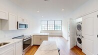 Located at 179 Chelsea Ave in Long Branch, NJ, this thoughtfully designed one-bedroom, one-bathroom unit offers a clean, modern aesthetic with high-quality finishes throughout. Warm hardwood-style flooring flows seamlessly across the entire single-floor layout, creating a cohesive and inviting atmosphere.

The kitchen is a standout feature, outfitted with crisp white shaker cabinetry, striking marble-look quartz countertops, and a full suite of stainless steel appliances including a range, over-the-range microwave, dishwasher, and refrigerator. A central island provides additional prep and dining space, while large multi-pane windows flood the area with natural light and offer views of the surrounding neighborhood.

The bedroom is a comfortable, well-proportioned retreat featuring a large built-in closet with custom shelving, hanging rods, and integrated drawers — offering excellent organization and storage. A wide window with a roller shade provides natural light and a neighborhood view.

The bathroom is finished with neutral large-format tile flooring, a white shaker vanity with quartz countertop, matte black hardware accents, and a backlit mirror, combining functionality with a refined contemporary style.

A hallway connects the living spaces efficiently. Throughout the unit, clean white walls, recessed lighting, and matte black hardware details contribute to a polished, modern character.