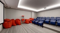 Located at 254 Phillip Street in Waterloo, Ontario, this dedicated screening room offers a polished, cinema-inspired amenity space designed for an immersive viewing experience. The room is finished with neutral grey walls and plush wall-to-wall carpet that contributes to both comfort and sound absorption. A defining architectural feature is the recessed tray ceiling fitted with soft, continuous LED cove lighting, which creates a warm, ambient glow without harsh overhead glare — perfectly suited to a screening environment. The focal point of the room is a large, wall-mounted projection screen paired with a ceiling-mounted projector, delivering a true theatre-quality picture. Seating is arranged in two tiered rows of classic blue upholstered theatre chairs, each equipped with armrests and cup holders, providing comfortable, unobstructed sightlines to the screen. Complementing the formal seating, a collection of oversized red bean bag chairs offers a more casual viewing option near the front. A vintage-style popcorn machine cart adds a fun, authentic touch to the cinematic atmosphere. Integrated wall-mounted surround sound speakers and in-wall control panels enhance the audio-visual setup, rounding out this well-equipped, self-contained screening room.
