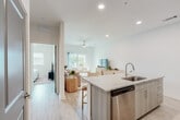 Located at 21101 Panama City Beach Pkwy in Panama City Beach, Florida, this single-story residence offers a clean, modern aesthetic defined by an open-concept floor plan and an abundance of natural light. The contemporary kitchen is well-appointed with light wood-toned cabinetry, granite countertops, a subway tile backsplash, and a full suite of stainless steel appliances including a refrigerator, range, microwave, and dishwasher. A peninsula with bar seating provides additional prep space and a casual dining option, while a separate in-unit laundry area adds everyday convenience. The open layout flows seamlessly from the kitchen into the combined dining and living area. The dining space accommodates a full table, while the living room features a ceiling fan, light wood-style flooring, and sliding glass doors that open to a private balcony, filling the space with natural light and outdoor views. The bedroom is a tranquil retreat with a walk-in closet and a ceiling fan, maintaining the home's consistent bright, neutral palette. Throughout, recessed lighting, light hardwood-style flooring, and crisp white walls create a cohesive, airy atmosphere well-suited to the coastal Panama City Beach setting.