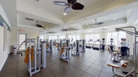 This fitness center offers a comprehensive, single-floor workout facility designed to accommodate a wide range of exercise needs. The main workout floor is generously sized, featuring tray ceilings with multiple ceiling fans that promote air circulation and comfort throughout. Large windows line the walls, flooding the space with abundant natural light and providing views of the surrounding exterior. Full-length mirrors are positioned along one wall, enhancing the sense of openness and allowing users to monitor their form during exercise.

The main floor is outfitted with a robust selection of professional-grade Cybex strength training machines, featuring padded yellow and tan seating, as well as multiple treadmills and cardio equipment arranged along the windowed wall. The flooring combines large-format tile with rubberized mat sections beneath the equipment, ensuring durability and safety.

An adjacent, glass-windowed room serves as a dedicated free weights area, visible from the main floor and accessible through French doors. This secondary space provides a more intimate setting for dumbbell and targeted strength work. A wall-mounted flat-screen television is also present, adding an entertainment option for users. The overall ambiance is clean, bright, and functional, reflecting a well-maintained facility built for serious fitness use.