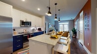 This thoughtfully designed single-floor residence blends contemporary style with functional living. The open-concept kitchen is a standout feature, showcasing bold navy lower cabinetry paired with crisp white upper cabinets, granite countertops, and gold-tone hardware and fixtures. A large central island with bar seating serves as an ideal gathering spot, illuminated by striking pendant lights overhead. Stainless steel appliances, including a French door refrigerator, built-in microwave, and electric range, complete the well-equipped cooking space.

The kitchen flows seamlessly into the living area, which is bathed in natural light from oversized French doors that open to a private balcony, offering views of the surrounding neighborhood. Warm hardwood flooring runs throughout the main living spaces, adding continuity and warmth.

The bedrooms are generously proportioned, each featuring large windows dressed with wood blinds and floor-length curtains. One bedroom features a deep teal accent wall, while another is finished in warm yellow tones, each creating a distinct and cozy atmosphere.

The primary bathroom features a walk-in glass shower with herringbone tile, a dual-sink vanity with granite countertops, navy cabinetry with gold hardware, and access to a dedicated walk-in closet. The overall ambiance is modern, vibrant, and comfortable.