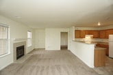 This single-floor residence offers a thoughtfully arranged layout that balances comfort and functionality throughout its key living areas. The spacious living room serves as the heart of the home, centered around a tile-surround fireplace flanked by large windows that invite natural light. A glass-paned exterior door provides direct outdoor access, adding to the room's open, airy feel. Adjacent to the living area, an open-concept space connects to the kitchen via a raised breakfast bar with a dark countertop, creating a natural flow between the two zones. The kitchen is well-equipped with warm oak cabinetry, light countertops, a white appliance suite including a range and refrigerator, and durable tile flooring. The bedrooms are carpeted in neutral tones and feature windows for natural light and individual closets for ample storage. The bathrooms are finished with tile flooring, one offering a full tub-and-shower combination with a grab bar and a built-in shelving closet nearby, while the other provides a vanity with a medicine cabinet mirror. Throughout the residence, a consistent palette of soft neutral tones and clean white trim contributes to a bright, move-in-ready ambiance.