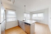 Located at 1 E Main, Unit 609 in Bound Brook, NJ, this thoughtfully designed one-bedroom, one-bathroom residence offers a clean, modern aesthetic throughout. The open-concept layout seamlessly connects the living room, dining area, and kitchen, creating an inviting and functional living space. Light wood-tone flooring runs throughout, complementing the bright white walls and abundant natural light from multiple windows with views of the surrounding area.

The kitchen is a standout feature, centered around a large island with striking marble-veined quartz countertops and a double undermount sink. Sleek gray cabinetry, a white hexagonal tile backsplash, and a full suite of stainless steel appliances — including a refrigerator, range, microwave, and dishwasher — complete the space with a polished, contemporary feel. A pendant light anchors the island with style.

The bedroom is a comfortable, well-lit retreat with a window offering outdoor views and access to a closet. A flexible den provides additional space for a home office or guest room. The bathroom features a frameless glass walk-in shower with large-format tile. Additional conveniences include in-unit laundry and two closets for ample storage throughout.