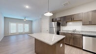 Located at 3400 Tevis Dr. in Louisville, KY, this well-appointed single-story home offers three bedrooms, two bathrooms, and a thoughtfully designed open-concept layout. The kitchen is a standout centerpiece, featuring rich dark wood cabinetry, granite countertops, white subway tile backsplash, a central island with pendant lighting, and a full suite of stainless steel appliances including a refrigerator, range, microwave, and dishwasher. Light wood-style flooring flows seamlessly throughout the home, creating a cohesive and modern aesthetic. The living area is bright and open, benefiting from natural light through large windows and a glass door that leads to the exterior. Ceiling fans are present in the living and bedroom areas for added comfort. The primary bedroom is generously sized and includes a walk-in closet outfitted with wire shelving for practical storage. Both bathrooms are finished with granite-topped dark wood vanities and large-format tile flooring. One bathroom features a glass-enclosed walk-in shower with subway tile surround. Additional bedrooms are well-proportioned, each with light-filled windows and ceiling fans. Two dedicated closets provide ample storage throughout the home. The overall design balances modern finishes with a clean, neutral palette.