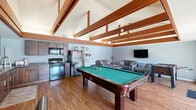Located at 2950 W Portage Bay Ave in Davis, California, this single-floor community clubhouse offers a versatile and welcoming environment designed for both recreation and relaxation. The space is defined by striking architectural elements, including vaulted ceilings with bold exposed wooden beams that lend warmth and character throughout.

The main gathering area seamlessly integrates a living room, dining space, and kitchen. The living room features comfortable sectional seating, a wall-mounted television, and warm hardwood flooring topped with a colorful area rug, creating an inviting lounge atmosphere. A full-size pool table serves as a central recreational focal point, while a classic red popcorn machine adds a playful, social touch. The kitchen is equipped with dark wood cabinetry and full appliances, providing practical amenities for events and gatherings. A glass-top dining table with leather chairs completes the social area.

Large sliding glass and French doors open directly to an outdoor area, filling the interior with abundant natural light and offering seamless access to the pool and patio space beyond.

The dedicated exercise room is well-equipped with treadmills, an elliptical, cable machine, and a weight bench, all set on durable rubber flooring. Exposed beams, a ceiling fan, a wall-mounted TV, and direct outdoor access make this fitness space both functional and comfortable.