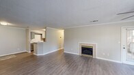 Located at 117 Royal Dr in Madison, Alabama, this single-story, 4-bedroom, 2-bathroom home offers a well-designed layout with a comfortable and functional living environment. The living room serves as the heart of the home, highlighted by a classic tile-surround fireplace with brass accents and durable hardwood-style flooring that flows seamlessly throughout the main areas. Crown molding and a textured ceiling add a refined architectural touch, while the open sightlines to the kitchen create an inviting, connected feel. The kitchen is well-appointed with gray cabinetry, light stone-look countertops, a full suite of black appliances including a refrigerator, electric range, and built-in microwave, plus a peninsula that opens to the living area. The bedrooms feature plush carpeting, natural light from windows with blinds, and generous closet space, including a walk-in closet with wire shelving. The bathrooms are finished with gray vanities, light countertops, and tiled shower/tub combos with wood-style flooring. A dedicated laundry room with wire shelving and side-by-side washer and dryer hookups adds everyday convenience. A separate bedroom wing offers a bright, open room with a ceiling fan and multiple windows, ideal as a primary suite or flex space.