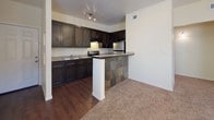 This single-story residence offers a cohesive layout that balances functional design with comfortable living. The kitchen serves as a visual centerpiece, featuring rich dark-stained cabinetry, granite-style countertops with a mosaic tile backsplash, stainless steel appliances including a gas range and refrigerator, and a peninsula breakfast bar wrapped in slate-style tile. Wood-style flooring runs throughout the kitchen and entry areas, providing a warm, durable foundation.

The open living area transitions seamlessly from the kitchen, featuring plush wall-to-wall carpeting, ceiling fans with light fixtures, and multiple windows that invite natural light. A closet with paneled doors adds convenient storage directly off the main living space.

The bedrooms are generously proportioned, each finished with soft carpeting, ceiling fans, and ample natural light. Closets are well-sized, with one bedroom featuring a walk-in closet with a hanging rod and upper shelving, and another offering a spacious reach-in closet. One bedroom provides direct access to a bathroom.

The bathrooms are finished consistently with dark vanity cabinetry, tile-accented countertops, and wood-style flooring. Each includes a full tub-shower combination with chrome fixtures and a tile surround border detail, completing a polished and practical interior.