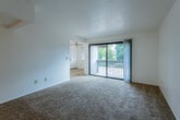 This single-floor residence offers a clean, functional layout with a cohesive neutral color palette throughout. The main living area is generously proportioned, featuring wall-to-wall carpet and crisp white walls with a textured ceiling. A large sliding glass door fills the space with natural light and opens directly onto a private balcony, offering pleasant outdoor views of surrounding greenery. An adjacent room, accessible through an open doorway, provides additional flexible living or sleeping space, also finished with carpet and ample wall space. The kitchen is a standout feature, outfitted with bright white shaker-style cabinetry, granite-patterned countertops, and light wood-look tile flooring. It includes a full suite of white appliances — a refrigerator, electric range, and dishwasher — along with a sink and generous storage both above and below the counters. The bathroom echoes the kitchen's clean aesthetic, with matching granite-patterned countertops on the vanity, tile flooring, and a full tub-shower combination with chrome fixtures. Throughout the residence, consistent finishes and a bright, airy atmosphere create a welcoming and practical living environment.