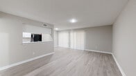 This 1-bedroom, 1-bathroom single-story unit offers a clean, modern aesthetic with light wood-look flooring and neutral gray tones carried throughout every room. The open-concept living and dining area is bright and welcoming, anchored by a wide sliding glass door fitted with vertical blinds that allow for adjustable natural light. A pass-through window connects the living space to the kitchen, enhancing the open feel. The galley-style kitchen is efficiently designed with white shaker cabinets, light stone countertops, a stainless steel double-basin sink, and black appliances including a refrigerator, range, and dishwasher. The spacious bedroom features a ceiling fan with light fixture and a window with outdoor views, providing both comfort and ventilation. A dedicated closet offers full-width shelving and hanging rods for ample storage. The bathroom is outfitted with a full tub-and-shower combination with white tile surround, a white vanity with stone countertop, and wood-look flooring that ties the space together. A hallway connects the private areas of the unit, completing a practical and cohesive floor plan suited for everyday living.