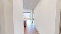 Located on the 14th floor in Dallas's vibrant Uptown neighborhood, this one-bedroom, one-bathroom residence offers a thoughtfully designed, modern living experience. Warm hardwood-style flooring flows throughout the open-concept layout, complementing the clean white walls and recessed lighting that give the space a bright, airy feel.

The kitchen is a standout feature, showcasing flat-front light wood cabinetry, quartz countertops, a center island with an undermount sink, and a full suite of stainless steel appliances including a refrigerator, microwave, and range. The open design allows the kitchen to connect seamlessly with the living area, creating an ideal space for entertaining.

The living area opens directly onto a private balcony through a sleek glass-paneled door, offering panoramic views of the Dallas skyline — a striking feature that fills the interior with natural light.

The bedroom is generously proportioned, featuring a tray ceiling with a ceiling fan, large floor-to-ceiling windows framing expansive city views, and hardwood-style flooring. The bathroom is elegantly appointed with a floating wood vanity, quartz countertop, a large framed mirror, a glass-enclosed shower with tile surround, and access to a walk-in closet with built-in shelving.