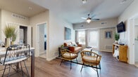 This single-story residence offers a thoughtfully designed layout that balances open-concept living with defined private spaces. The living room serves as the heart of the unit, featuring wood-style flooring, vaulted ceilings, and a ceiling fan with integrated lighting. Natural light enters through a set of front-facing windows and a glass-paneled door, while neutral walls provide a versatile backdrop. The space comfortably accommodates multiple seating arrangements and connects openly to adjacent areas.

The kitchen is well-equipped with dark, rich cabinetry extending to the upper walls, black appliances including a refrigerator, range, and over-the-range microwave, and light countertops that provide contrast. A freestanding island with seating offers casual dining and additional prep space. Wood-style flooring continues throughout this area, maintaining visual cohesion.

The bedroom is a calm retreat finished with plush carpeting and a large window dressed with curtains, allowing natural light while maintaining privacy. Two sets of double closet doors provide generous storage capacity.

The bathroom features a wide vanity with dark cabinetry, a large mirror, and wood-style flooring, offering a clean and functional design. Overall, the unit presents a modern, cohesive aesthetic throughout.