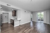 Located at 2200 Colorado Ave in Santa Monica, CA, this thoughtfully designed one-bedroom, one-bathroom residence offers a clean, contemporary aesthetic throughout. The open-concept living and kitchen area is anchored by rich hardwood-style flooring and neutral gray tones, creating a bright and cohesive atmosphere. A sliding glass door leads to a private balcony, bringing in ample natural light and views of lush surrounding greenery — a hallmark of the Southern California setting.

The kitchen is well-equipped with dark espresso cabinetry, white countertops, stainless steel appliances including a range, microwave, refrigerator, and dishwasher, all illuminated by recessed lighting. A peninsula counter connects the kitchen seamlessly to the living area.

The bedroom is a comfortable, well-lit retreat featuring dual windows that frame outdoor palm and tropical foliage views, complemented by the same hardwood-style flooring. A dedicated closet provides convenient storage. The bathroom is finished with dark vanity cabinetry, a white countertop, and a backlit mirror, offering a clean and modern look. A built-in shelving unit adds practical storage. The unit also includes an additional closet off the living area, maximizing functionality throughout this efficient Santa Monica residence.