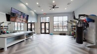 Located at 2501 S 4th St in Louisville, Kentucky, this single-floor resident fitness center is thoughtfully designed to support a comprehensive workout experience. The facility is organized into several distinct training zones, each tailored to a specific type of exercise.

The open functional training studio serves as the centerpiece of the space, featuring herringbone-patterned luxury vinyl flooring, recessed lighting, a ceiling fan, and a wall-mounted flat-screen TV. Large windows and glass double doors flood the area with natural light and offer views of the surrounding neighborhood. The studio is equipped with a TRX suspension system, resistance bands, weighted balls, a punching bag, and balance equipment, providing ample options for functional and high-intensity workouts.

A dedicated cardio room houses multiple treadmills, ellipticals, and a stair climber, each equipped with individual screens. Natural light from double-hung windows brightens the space, and dark rubber flooring provides a durable, performance-ready surface.

The strength training area features cable machines and selectorized equipment positioned in front of large wall mirrors, which enhance the sense of space and allow for form monitoring. A wall-mounted TV adds an entertainment element to this zone.

A separate cycling and boxing studio includes spin bikes and a heavy bag, accented by framed artwork on the walls and herringbone flooring. Additional amenities include a water fountain and bottle-filling station, reinforcing the facility's focus on resident wellness and convenience.
