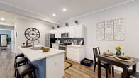 Located at 3535 SW 20th St in Ocala, Florida, this single-story residence at Pointe Grand Ocala showcases a modern, cohesive design with warm wood-look flooring, crown molding, and recessed lighting flowing throughout. The open-concept kitchen is a standout feature, outfitted with crisp white shaker cabinetry, bright white quartz countertops, a bold navy blue subway tile backsplash, and stainless steel appliances. A central island with a contrasting blue base and bar seating adds both functionality and visual interest, while an adjacent dining area provides a seamless transition for entertaining. The living room offers a relaxed, comfortable layout with access to a private exterior door that lets in natural light. Crown molding and neutral-toned walls lend a clean, polished feel to the space. The bedrooms are well-proportioned, each featuring wood-look flooring, ample closet storage, and soft natural light from windows with window treatments. The bathroom is finished with white shaker-style cabinetry, a white countertop vanity, and wood-look flooring that ties into the home's overall aesthetic. The residence carries a welcoming, contemporary ambiance suitable for everyday living.