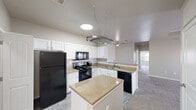 Located at 14681 S 82nd E Ave in Bixby, Oklahoma, this single-floor, three-bedroom, two-bathroom home offers a practical and comfortable layout across a well-utilized footprint. The kitchen serves as a central highlight, featuring crisp white shaker cabinetry, granite-style countertops, a subway tile backsplash, and a full suite of black appliances including a refrigerator, electric range, microwave, and dishwasher. A center island provides additional prep space and storage, while a decorative hanging pot rack overhead adds a functional design touch. Wood-look vinyl flooring runs through the kitchen and entry areas, transitioning to plush carpet in the living and bedroom spaces. The primary bedroom is generously sized and features a tray ceiling with crown molding detail, a ceiling fan, a private door to an outdoor balcony or patio, and a walk-in closet with built-in wire shelving. Additional bedrooms are carpeted and well-lit with natural light from windows fitted with blinds. The bathrooms include granite-topped vanities and a tub/shower combination with clean white surround. A dedicated laundry room with side-by-side washer and dryer hookups and built-in shelving adds everyday convenience. Three closets throughout the home provide ample storage.