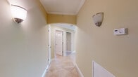 This single-story residence showcases a cohesive design throughout, characterized by warm beige tones, white trim, and arched doorways that lend an elegant, classical feel to the interior. The hallways are finished with diagonal-set tile flooring and crown molding, with wall sconces providing ambient lighting as you move through the space.

The open-concept living and dining area features plush carpeting, crown molding, a ceiling fan, and large sliding glass doors that allow generous natural light and outdoor views. This area connects seamlessly to the kitchen, which is outfitted with rich honey-toned wood cabinetry, dark granite countertops with subtle patterning, a stainless steel double sink, and a windowed breakfast bar that overlooks the living space.

The bedrooms are carpeted and include arched double-door closets with built-in shelving for organized storage. The bathroom features warm wood vanity cabinetry, a light countertop, large tile flooring, and a well-lit mirror above the sink. A dedicated laundry room provides tile flooring, built-in shelving, and hookups for added convenience. Overall, the space presents a comfortable, well-detailed interior with consistent finishes throughout.