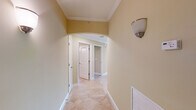 This single-story residence showcases a cohesive design throughout, characterized by warm beige tones, white trim, and arched doorways that lend an elegant, classical feel to the interior. The hallways are finished with diagonal-set tile flooring and crown molding, with wall sconces providing ambient lighting as you move through the space.

The open-concept living and dining area features plush carpeting, crown molding, a ceiling fan, and large sliding glass doors that allow generous natural light and outdoor views. This area connects seamlessly to the kitchen, which is outfitted with rich honey-toned wood cabinetry, dark granite countertops with subtle patterning, a stainless steel double sink, and a windowed breakfast bar that overlooks the living space.

The bedrooms are carpeted and include arched double-door closets with built-in shelving for organized storage. The bathroom features warm wood vanity cabinetry, a light countertop, large tile flooring, and a well-lit mirror above the sink. A dedicated laundry room provides tile flooring, built-in shelving, and hookups for added convenience. Overall, the space presents a comfortable, well-detailed interior with consistent finishes throughout.