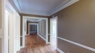 This single-floor residence showcases a wealth of classic architectural character that speaks to its heritage. Throughout the main living areas, rich hardwood floors gleam underfoot while elaborate crown molding and decorative wall paneling with white-trimmed picture frames lend an air of traditional elegance. Ornate ceiling medallions and textured ceiling finishes further highlight the craftsmanship embedded in the home's design.

The generously proportioned living and dining areas are bathed in natural light streaming through multiple large windows, some featuring transom panes that add to the period charm. White-trimmed wall panel moldings carry consistently through each room, creating a cohesive and refined aesthetic. A ceiling fan with a light fixture serves one of the main rooms, adding both function and a classic touch.

The kitchen is equipped with white cabinetry featuring raised-panel doors, warm-toned countertops, a stainless steel sink, and a freestanding gas range. Tile flooring grounds the space, and a large window provides ample natural light.

Two full bathrooms are present, each outfitted with a bathtub and shower combination, pedestal or wall-mounted sink, and toilet. One bathroom retains a classic cast-iron radiator, a nod to the home's historic roots. Throughout, the warm taupe wall palette ties the interior together into a cohesive, timeless presentation.