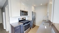 This single-floor unit has been carefully updated with a clean, contemporary aesthetic throughout. The kitchen is a standout feature, showcasing a two-tone design with crisp white upper cabinetry and contrasting dark lower cabinets, all complemented by sleek gray quartz countertops and a classic subway tile backsplash. A full suite of stainless steel appliances — including a gas range, over-the-range microwave, and a French door refrigerator with water dispenser — rounds out the functional and stylish cooking space. Light wood-look flooring flows consistently throughout the unit, adding warmth and visual continuity. The living areas are bright and open, with multiple windows dressed in horizontal blinds that allow generous natural light to filter in. Neutral warm-gray and white wall tones create a calm, versatile backdrop adaptable to various design styles. The bedroom features a large window, a sliding closet with track lighting, and the same durable wood-look flooring. The bathroom is a refined space highlighted by marble-look tile surround in the tub/shower combination, accented with a decorative mosaic tile border and a built-in niche, all finished with brushed nickel fixtures for a polished, cohesive look.