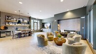 Located at 5401 Commonwealth Centre Pkwy in Midlothian, Virginia, this thoughtfully designed single-floor community amenity space offers a generous and versatile layout that seamlessly blends social and recreational functions. The interior is anchored by a warm, contemporary aesthetic, featuring sage-green accent walls, light herringbone-patterned hardwood flooring, and recessed lighting throughout.

The main lounge area invites relaxed gathering with plush swivel chairs, a tufted built-in sofa, and a textured stone accent wall with backlit display shelving. Large floor-to-ceiling glass panels and French doors flood the space with natural light and provide views to adjacent areas, enhancing the open, airy feel.

A dedicated billiards room, accessible via a sliding barn door, offers a full-size pool table set atop a patterned area rug, complemented by geometric pendant lighting and natural window light. Adjacent to this is a charming dining nook, distinguished by a bold patterned tile accent wall, open wooden shelving with curated décor, and pendant lighting over a communal dining table.

Near the entrance, a well-appointed coffee and refreshment bar features light cabinetry, a white countertop, and beverage equipment beneath a striking equestrian art piece. The overall ambiance is polished yet welcoming, making this an ideal space for socializing and community engagement.