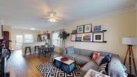 This two-story space offers four bedrooms and four bathrooms across a well-organized layout. The main living area features warm hardwood flooring, crown molding, and a ceiling fan, creating an inviting atmosphere. Picture ledges display framed artwork along the neutral-toned walls, while natural light filters through multiple windows dressed with sheer curtains. The dining area sits adjacent to the living room, providing a seamless flow between spaces.

The kitchen is equipped with stainless steel appliances, rich dark wood cabinetry with a built-in wine rack, and light hardwood floors. A set of French doors opens directly onto a balcony, offering outdoor views and bringing additional natural light into the space.

A carpeted staircase with a metal handrail and wall sconce lighting connects the two floors, with windows along the stairwell adding brightness to the transition between levels. The bedrooms feature carpet flooring and ceiling fans, with ample natural light from well-positioned windows. Each of the four bathrooms includes a shower with curtain, tile flooring, and a vanity with storage. The overall ambiance throughout the space is bright, neutral, and functional.