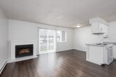 This single-floor residential unit offers a practical and comfortable layout across several well-defined spaces. The living room serves as the heart of the unit, featuring a white brick fireplace as a focal point, warm hardwood-style flooring, a baseboard heating system, and a textured ceiling. A sliding glass door flanked by vertical blinds fills the room with natural light and provides access to the outdoors.

Adjacent to the living area, the kitchen is designed for efficiency. It includes a peninsula countertop with a granite-style surface, a white electric coil cooktop, a dishwasher, a refrigerator, and a double sink — all set beneath ample white upper cabinetry. A range hood is positioned above the cooktop, and recessed ceiling fixtures provide consistent overhead lighting.

The bathroom is clean and straightforward, featuring a full-sized soaking tub with a shower rod, a toilet, and warm-toned hardwood-style flooring — offering a practical and functional space.

The bedroom is a quiet, well-proportioned room finished with plush wall-to-wall carpet in a neutral tone and a textured ceiling, providing a comfortable retreat. Throughout the unit, neutral color palettes, consistent flooring materials, and clean white trim create a cohesive and move-in-ready aesthetic.