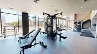 Located at 394 West Ave in Norwalk, CT, this two-floor fitness facility offers a comprehensive and well-appointed exercise environment spanning a generous total area across both levels. The main floor commands immediate attention with soaring double-height ceilings and floor-to-ceiling windows that flood the space with natural light while providing open views of the surrounding streetscape. This level houses an extensive cardio zone equipped with treadmills, ellipticals, stair climbers, and rowing machines, all positioned to take advantage of the expansive glazing. A dedicated strength training area features multi-station cable machines, free weights, benches, and wall-length mirrors, complemented by rubber flooring for safety and durability. A wooden staircase with distinctive vertical slat railings connects to the upper mezzanine level, which offers a more intimate exercise area with polished concrete floors, stationary bikes, and a striking large-scale map mural as a design focal point. Exposed ductwork and industrial-style ceilings lend the upper level a modern, urban aesthetic. A separate studio room features hardwood floors, full mirrored walls, built-in wooden benching, and integrated display screens, ideal for group fitness or individual training sessions. Together, the two floors create a dynamic, light-filled fitness destination.