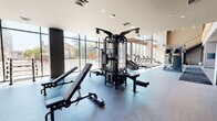 Located at 394 West Ave in Norwalk, CT, this two-floor fitness facility offers a comprehensive and well-appointed exercise environment spanning a generous total area across both levels. The main floor commands immediate attention with soaring double-height ceilings and floor-to-ceiling windows that flood the space with natural light while providing open views of the surrounding streetscape. This level houses an extensive cardio zone equipped with treadmills, ellipticals, stair climbers, and rowing machines, all positioned to take advantage of the expansive glazing. A dedicated strength training area features multi-station cable machines, free weights, benches, and wall-length mirrors, complemented by rubber flooring for safety and durability. A wooden staircase with distinctive vertical slat railings connects to the upper mezzanine level, which offers a more intimate exercise area with polished concrete floors, stationary bikes, and a striking large-scale map mural as a design focal point. Exposed ductwork and industrial-style ceilings lend the upper level a modern, urban aesthetic. A separate studio room features hardwood floors, full mirrored walls, built-in wooden benching, and integrated display screens, ideal for group fitness or individual training sessions. Together, the two floors create a dynamic, light-filled fitness destination.