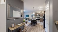 This thoughtfully designed 2-bedroom, 2-bathroom residence spans a single floor and features a contemporary open-concept layout that seamlessly connects the kitchen, dining, and living areas. The kitchen is a standout, boasting rich taupe cabinetry, marble-style countertops, a decorative tile backsplash, stainless steel appliances, and a central island with bar seating illuminated by pendant lighting. Wood-look flooring flows throughout the main living areas, adding warmth and continuity. The living room is bright and inviting, featuring a sliding glass door that opens to a private balcony with green outdoor views, and plush carpeting underfoot. The generously sized primary bedroom offers large windows with sheer drapery that invite natural light, along with soft carpeting and a closet. The second bedroom is equally well-sized, featuring carpeted floors and built-in closet storage. Both bathrooms display distinct design personalities — one with bold navy blue walls and a tub-shower combo over wood-look flooring, and the other styled in cool charcoal grey tones. The entry area features an accent wall in grey, creating a defined and stylish transition into the main living space.
