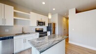 Located at 818 Robbie View in Colorado Springs, Colorado, this single-floor residence offers a clean, contemporary design with a cohesive aesthetic carried throughout every room. The kitchen serves as the heart of the home, boasting white shaker-style cabinetry, striking granite countertops with bold veining, a central island with pendant lighting, and a full suite of stainless steel appliances including a gas range, built-in microwave, and refrigerator. Light hardwood-style flooring runs seamlessly throughout the space, complementing the neutral warm-toned walls and crisp white trim. A well-proportioned hallway connects the living areas to the private spaces, with recessed lighting providing consistent illumination. The bathroom features matching granite countertops, white cabinetry, a tub-shower combination, and the same light flooring found throughout the home, creating a unified and polished look. Additional rooms offer flexible use, with high clerestory windows bringing in natural light while maintaining privacy. The open-concept kitchen and living area benefits from a sliding glass door that invites natural light and provides outdoor access. Overall, the space presents a bright, modern, and move-in-ready environment well-suited for comfortable everyday living in Colorado Springs.