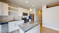 Located at 818 Robbie View in Colorado Springs, Colorado, this single-floor residence offers a clean, contemporary design with a cohesive aesthetic carried throughout every room. The kitchen serves as the heart of the home, boasting white shaker-style cabinetry, striking granite countertops with bold veining, a central island with pendant lighting, and a full suite of stainless steel appliances including a gas range, built-in microwave, and refrigerator. Light hardwood-style flooring runs seamlessly throughout the space, complementing the neutral warm-toned walls and crisp white trim. A well-proportioned hallway connects the living areas to the private spaces, with recessed lighting providing consistent illumination. The bathroom features matching granite countertops, white cabinetry, a tub-shower combination, and the same light flooring found throughout the home, creating a unified and polished look. Additional rooms offer flexible use, with high clerestory windows bringing in natural light while maintaining privacy. The open-concept kitchen and living area benefits from a sliding glass door that invites natural light and provides outdoor access. Overall, the space presents a bright, modern, and move-in-ready environment well-suited for comfortable everyday living in Colorado Springs.