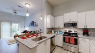 This thoughtfully designed 1-bedroom, 1-bathroom residence offers a smart and functional single-floor layout. The open-concept kitchen and living room serve as the heart of the home, featuring striking granite countertops, crisp white cabinetry, and a full suite of stainless steel appliances including a refrigerator, range, microwave, and dishwasher. A peninsula with bar seating provides a casual dining option and naturally connects the kitchen to the living area. Soaring ceilings amplify the sense of space throughout, while hardwood-style flooring in the main living areas adds warmth and continuity. The living room is bright and airy, with a sliding glass door that invites natural light and opens to an outdoor area with views of surrounding greenery. The bedroom features plush carpeting, a large window with outdoor views, and access to a dedicated closet. The full bathroom is finished with tile flooring, a granite-topped vanity with rich wood cabinetry, and a tub-shower combination. Pendant lighting over the kitchen peninsula and generous vertical wall space throughout the unit contribute to a modern, clean aesthetic that balances style with everyday practicality.