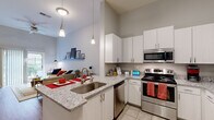 This thoughtfully designed 1-bedroom, 1-bathroom residence offers a smart and functional single-floor layout. The open-concept kitchen and living room serve as the heart of the home, featuring striking granite countertops, crisp white cabinetry, and a full suite of stainless steel appliances including a refrigerator, range, microwave, and dishwasher. A peninsula with bar seating provides a casual dining option and naturally connects the kitchen to the living area. Soaring ceilings amplify the sense of space throughout, while hardwood-style flooring in the main living areas adds warmth and continuity. The living room is bright and airy, with a sliding glass door that invites natural light and opens to an outdoor area with views of surrounding greenery. The bedroom features plush carpeting, a large window with outdoor views, and access to a dedicated closet. The full bathroom is finished with tile flooring, a granite-topped vanity with rich wood cabinetry, and a tub-shower combination. Pendant lighting over the kitchen peninsula and generous vertical wall space throughout the unit contribute to a modern, clean aesthetic that balances style with everyday practicality.