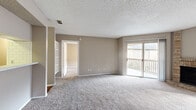 This single-floor residence offers a practical and comfortable layout across two bedrooms, two bathrooms, and a well-connected set of living spaces. The spacious living room is finished with plush carpeting and neutral taupe walls, and features built-in shelving along one wall. Large sliding glass doors open directly onto a covered balcony, allowing natural light to fill the room and providing outdoor views. A pass-through connects the living area to the galley-style kitchen, which is equipped with white cabinetry, a white tile backsplash, hardwood flooring, and a full suite of white appliances including an electric range. The primary bedroom is generously sized with soft carpet, a ceiling fan with light fixture, a natural light window with blinds, and direct access to a walk-in closet outfitted with built-in shelving and hanging rods. The second bedroom mirrors the comfortable feel with carpet, a ceiling fan, and a window. Both bathrooms are clean and functional; one features a full tub-shower combination unit with chrome fixtures and hardwood-style flooring. Two closets throughout the unit provide ample storage. The textured ceilings and consistent neutral color palette give the space a cohesive, move-in ready appearance throughout.