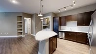 Located at 5350 Burnet Rd in Austin, TX, this well-appointed 2-bedroom, 2-bathroom residence offers a thoughtfully designed single-level floor plan. The open-concept kitchen and living area serves as the heart of the home, featuring rich dark-stained cabinetry, stainless steel appliances including a refrigerator, range, microwave, and dishwasher, white subway tile backsplash, and a curved center island with a white countertop illuminated by pendant lighting. Track lighting overhead adds a modern touch. A dedicated in-unit laundry alcove with a washer and dryer provides added convenience just off the kitchen. The living area is bathed in natural light through a sweeping curved bay of windows and a glass door, complemented by hardwood-style flooring and a ceiling fan. The spacious primary bedroom offers a generous footprint, hardwood-style flooring, and access to a well-sized closet. Built-in shelving in the living area provides practical storage. The bathrooms are finished with tile flooring, dark wood vanities, white countertops, and dual round mirrors. Neutral gray-toned walls throughout create a cohesive, modern aesthetic across the entire residence.