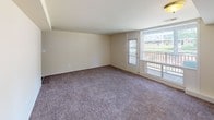 This single-floor unit offers a practical and comfortable layout across several interconnected rooms. The kitchen is designed for efficiency, featuring warm medium-toned wood cabinetry on both upper and lower levels, dark laminate countertops, and white appliances including a coil-burner range and a full-size refrigerator. Wood-look vinyl plank flooring runs throughout the kitchen, adding a clean, durable surface underfoot.

The living area is generously proportioned, with neutral-toned carpet providing a soft, comfortable foundation. The room is bright and open, with smooth white walls and flush ceiling lighting. A door and large window provide access to an outdoor balcony that overlooks a neighboring residential area, bringing in natural light and a sense of openness.

The bathroom is finished with white square tile that extends along the lower walls and into the tub surround, complemented by dark wood-look flooring. A pedestal sink, mirrored medicine cabinet with overhead lighting, and a full tub with a shower complete the space with a clean, classic aesthetic.

Overall, the unit maintains a neutral, move-in-ready character with consistent finishes throughout.