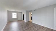 Located at 2415 West, this single-floor residence offers a clean, open layout designed for practical and comfortable living. The main living area is a standout feature, showcasing wide-plank, wood-look flooring in a warm gray-brown tone that runs throughout the space, lending a modern yet inviting feel. Light gray walls provide a neutral backdrop that enhances the sense of openness and pairs well with the natural light streaming in through a large front-facing window. A stylish pendant light fixture adds a subtle decorative touch near the entryway, which features a classic white front door framed by clean white trim and baseboards. The textured ceiling adds a layer of architectural character to the otherwise streamlined interior. Visible from the main living space, doorways lead to additional rooms, including what appears to be a kitchen outfitted with dark appliances, suggesting a well-equipped and functional culinary space. HVAC venting is integrated into the ceiling, ensuring year-round climate comfort. The overall ambiance of this single-story home is bright, neutral, and move-in ready, with a straightforward layout that maximizes usable space across the floor plan.