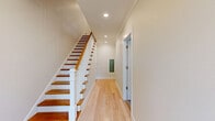 This three-story townhome in Charlotte's 28209 zip code offers a well-designed layout across three distinct floors. The entry-level garage provides convenient parking alongside utility space and staircase access to the main living areas. The primary living floor features an open-concept kitchen and living room, where crisp white shaker cabinetry, a large quartz-topped island with pendant lighting, stainless steel appliances, and light hardwood floors combine to create a bright, functional space with natural light from multiple windows. Elegant crown molding and recessed lighting add refined detail throughout. Upstairs, three bedrooms include a generous primary suite with a ceiling fan, plush carpeting, a private en-suite bathroom, and ample closet space with custom built-in shelving and hanging rods. The five bathrooms are thoughtfully appointed, with one showcasing floor-to-ceiling vertically stacked tile and a glass-enclosed shower. A dedicated laundry room with full-size washer and dryer adds everyday convenience. Hallways are finished with warm hardwood floors, and the staircase features classic white balusters with rich wood treads. Residents also enjoy an outdoor balcony with views of the surrounding community.