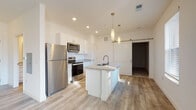 Located at 210 W Fifth Ave in Columbus, Ohio, this single-floor unit offers a thoughtfully designed open-concept layout with modern finishes throughout. The kitchen serves as a central highlight, featuring white shaker cabinetry, granite countertops, a large center island with an undermount sink, and a full suite of stainless steel appliances including a refrigerator, range, and over-the-range microwave. Stylish pendant lighting and a distinctive sliding barn door add character to the space. Light wood-look flooring flows throughout the main living areas, creating a cohesive and contemporary aesthetic. The living area is bright and welcoming, benefiting from large windows and a glass-paned exterior door that invite natural light and provide outdoor views. The bedroom is carpeted for comfort and offers generous proportions, complemented by a spacious walk-in closet with built-in wire shelving for ample storage. The bathroom continues the refined design language with granite countertops, white cabinetry, and wood-look flooring. Recessed lighting throughout enhances the clean, modern ambiance of the entire unit. The overall design emphasizes functionality and style, making this a well-appointed space in the heart of Columbus.