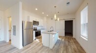 Located at 210 W Fifth Ave in Columbus, Ohio, this single-floor unit offers a thoughtfully designed open-concept layout with modern finishes throughout. The kitchen serves as a central highlight, featuring white shaker cabinetry, granite countertops, a large center island with an undermount sink, and a full suite of stainless steel appliances including a refrigerator, range, and over-the-range microwave. Stylish pendant lighting and a distinctive sliding barn door add character to the space. Light wood-look flooring flows throughout the main living areas, creating a cohesive and contemporary aesthetic. The living area is bright and welcoming, benefiting from large windows and a glass-paned exterior door that invite natural light and provide outdoor views. The bedroom is carpeted for comfort and offers generous proportions, complemented by a spacious walk-in closet with built-in wire shelving for ample storage. The bathroom continues the refined design language with granite countertops, white cabinetry, and wood-look flooring. Recessed lighting throughout enhances the clean, modern ambiance of the entire unit. The overall design emphasizes functionality and style, making this a well-appointed space in the heart of Columbus.