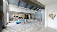 This single-floor lobby showcases a thoughtfully designed interior that blends coastal and contemporary aesthetics. The space is defined by its striking exposed dark wood beams set against a vivid blue ceiling, creating a dramatic architectural contrast with the otherwise light and airy surroundings. Large-format patterned tile flooring anchors the space, featuring a subtle swirling motif that adds visual texture underfoot.

The reception desk runs prominently along the back wall, finished with warm wood paneling and backlit displays, and equipped with multiple workstations to accommodate guests efficiently. Recessed lighting throughout ensures the space remains bright and inviting. A feature wall with alternating blue and natural wood horizontal panels adds a bold focal point near the entrance, complementing the overall coastal palette.

The seating area features a striped upholstered sofa in neutral tones paired with vibrant blue accent furniture and metallic side tables, striking a balance between comfort and style. Decorative sculptures and coastal artwork are tastefully placed throughout, reinforcing the design theme. The overall ambiance is open, polished, and welcoming, suited to a professional hospitality or commercial environment.