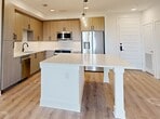 This 1,020-square-foot single-floor residence offers 2 bedrooms, 2 bathrooms, and 2 closets, delivering a thoughtfully designed modern living experience. The open-concept kitchen and living area serves as the heart of the home, showcasing light wood-grain cabinetry with matte black hardware, white quartz countertops, stainless steel appliances including a built-in microwave and dishwasher, and a large central island with pendant lighting overhead. A built-in beverage refrigerator adds a premium touch. Light wood-tone luxury vinyl plank flooring flows consistently throughout the entire unit, enhancing its cohesive, contemporary aesthetic. The primary bedroom measures 150 square feet and features a ceiling fan, direct balcony access via French doors offering open exterior views, and a dedicated walk-in closet with built-in shelving and hanging rods. The en-suite bathroom is a standout, featuring a bold blue vanity with dual sinks, matte black fixtures, an illuminated mirror, and a glass-enclosed tile shower. The second bedroom also includes a ceiling fan, a walk-in closet with built-in organization, and its own balcony access. A second full bathroom serves the additional bedroom. Recessed lighting and clean white walls complete the bright, modern ambiance throughout.