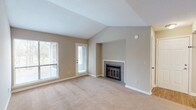This traditional 1-bedroom, 1-bathroom residence is laid out across a single floor, offering a well-organized and functional floor plan. The living room is a standout space, featuring vaulted ceilings that lend a sense of openness and volume. A tile-surround fireplace with a glass-front insert serves as the room's focal point, while large windows and a private exterior door allow natural light to flow in and provide direct outdoor access. Soft wall-to-wall carpeting runs throughout the living and bedroom areas, contributing to a warm and comfortable ambiance. The kitchen is appointed with warm oak cabinetry, dark granite-style countertops, hardwood-style flooring, and includes a dishwasher, range, and refrigerator. A pass-through window connects the kitchen to the adjacent dining area, which is highlighted by a classic chandelier. The bedroom is a quiet, well-proportioned retreat with its own window and plush carpeting. The bathroom is clean and straightforward, featuring a full tub-shower combination with chrome fixtures. Overall, the space presents a classic, traditional aesthetic with practical finishes throughout.