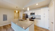 Located at 1545 Timberstop Street in Lancaster, Ohio, this single-floor home offers a thoughtfully designed layout with modern finishes throughout. The kitchen serves as a central highlight, featuring a large island with a granite countertop and built-in sink, illuminated by stylish pendant lighting. White shaker-style cabinetry lines the walls, complemented by stainless steel appliances including a refrigerator, electric range, and over-the-range microwave. Light wood-look flooring runs throughout the kitchen and entry areas, adding warmth and continuity. The open-concept design flows seamlessly into the living area, which is finished with plush neutral carpeting, creating a comfortable and inviting atmosphere. The bedrooms are generously sized with vaulted ceilings, soft carpet flooring, and large windows that allow natural light to fill the space while offering views of the surrounding neighborhood. The bathrooms are well-appointed, featuring granite-topped white vanities with undermount sinks. The primary bathroom includes a double vanity and a tub-shower combination, while the secondary bathroom offers a single vanity with a tub-shower unit. Recessed lighting and neutral wall tones throughout the home contribute to a clean, contemporary aesthetic.