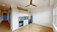 Located at 212 Melba St in Dallas, TX, this well-appointed 1-bedroom, 1-bathroom unit offers a thoughtfully designed single-floor layout with modern finishes throughout. The open-concept living, dining, and kitchen area serves as the heart of the home, anchored by striking herringbone-patterned hardwood flooring and a warm wood-blade ceiling fan that adds a stylish focal point. The kitchen features white flat-front cabinetry with under-cabinet lighting, a gray tile backsplash, stainless steel sink, built-in oven, and a stainless refrigerator — all designed for both function and aesthetics. A long hallway lined with charcoal-framed panel doors connects the main living area to the private spaces, including the bedroom, bathroom, two closets, and a laundry area. The bedroom is a comfortable, light-filled retreat with herringbone flooring and a ceiling fan. The walk-in closet includes built-in shelving and hanging rods, offering ample organization. The bathroom is finished in clean white tile with a modern vanity featuring matte black hardware and a round LED mirror. A private balcony provides outdoor access, completing this efficiently designed and contemporary urban residence.